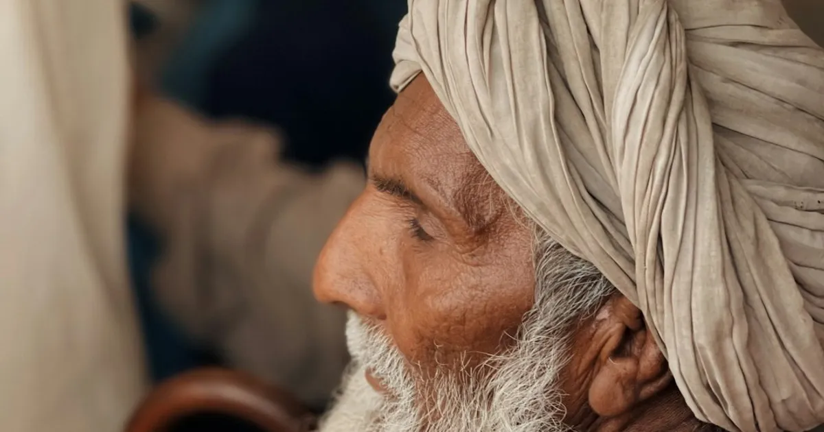 An elderly South Asian grandfather sitting in traditional attire deep in thought