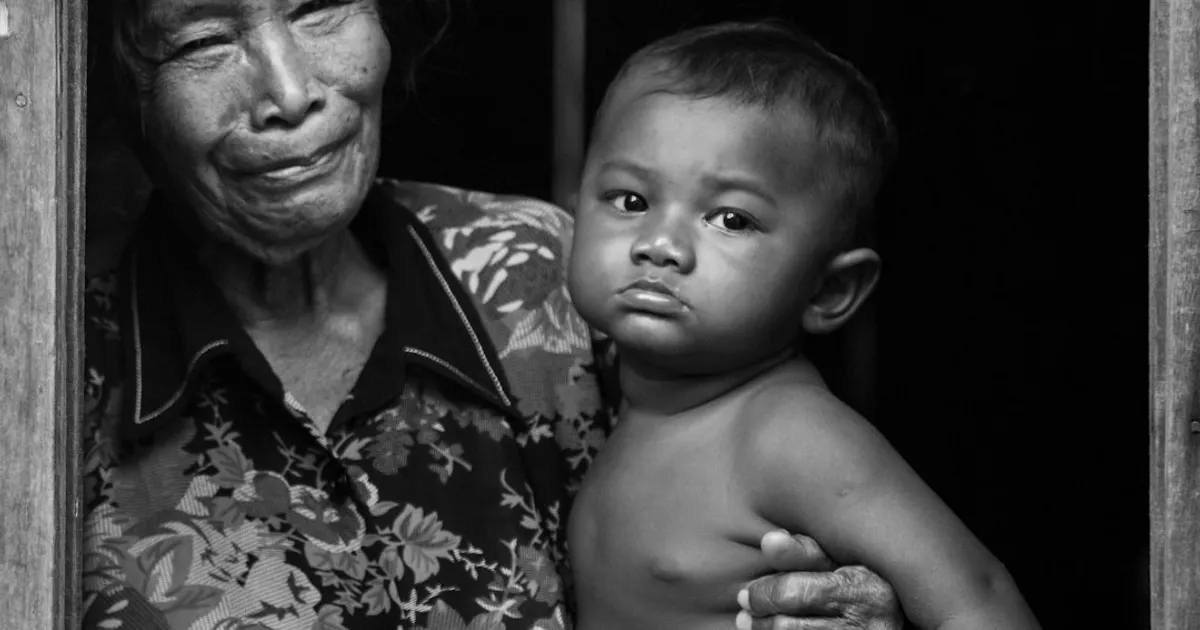 An elderly South Asian woman speaking warmly while a younger family member listens attentively over chai