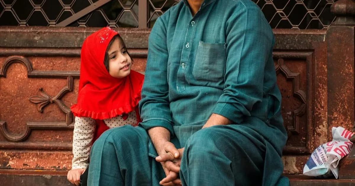 An elder South Asian man sharing stories with his family in a warm, traditional home setting