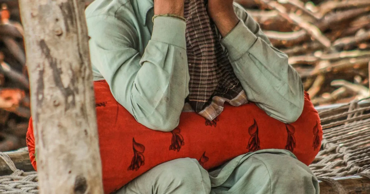 A Pakistani father in traditional attire sitting outdoors with a thoughtful expression, ready to share his life stories