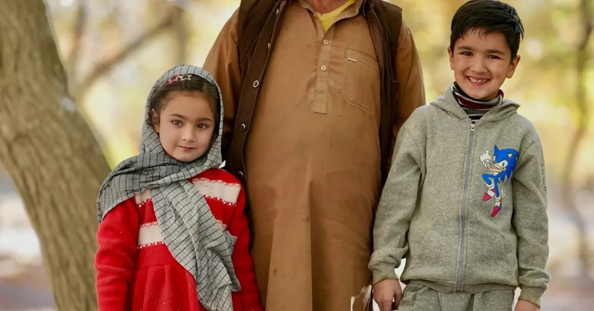 An elder from Gilgit Baltistan, Pakistan, standing with two children in an autumn park — a reminder that migration stories live between generations