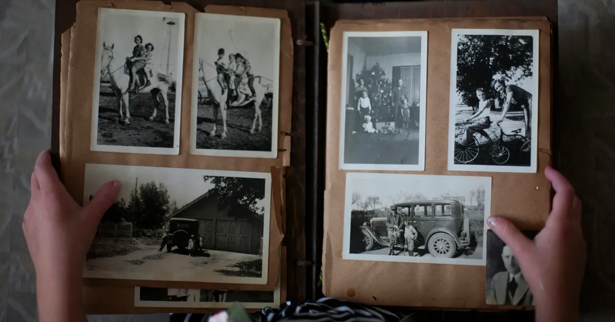 Person opening photo album displaying grayscale photographs for digitization and preservation