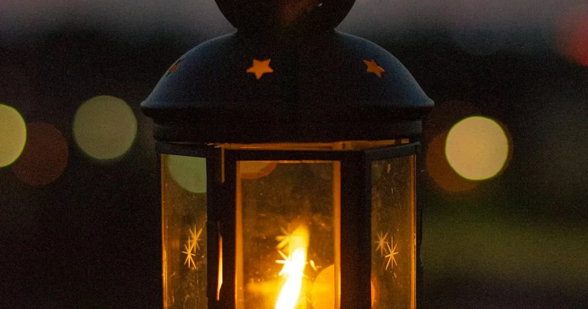 A warm memorial candle and glass lantern on a wooden table with a small photograph and handwritten note