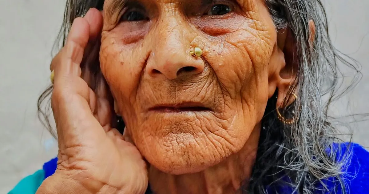 An elderly South Asian woman with grey hair, her face carrying decades of wisdom and gentle warmth